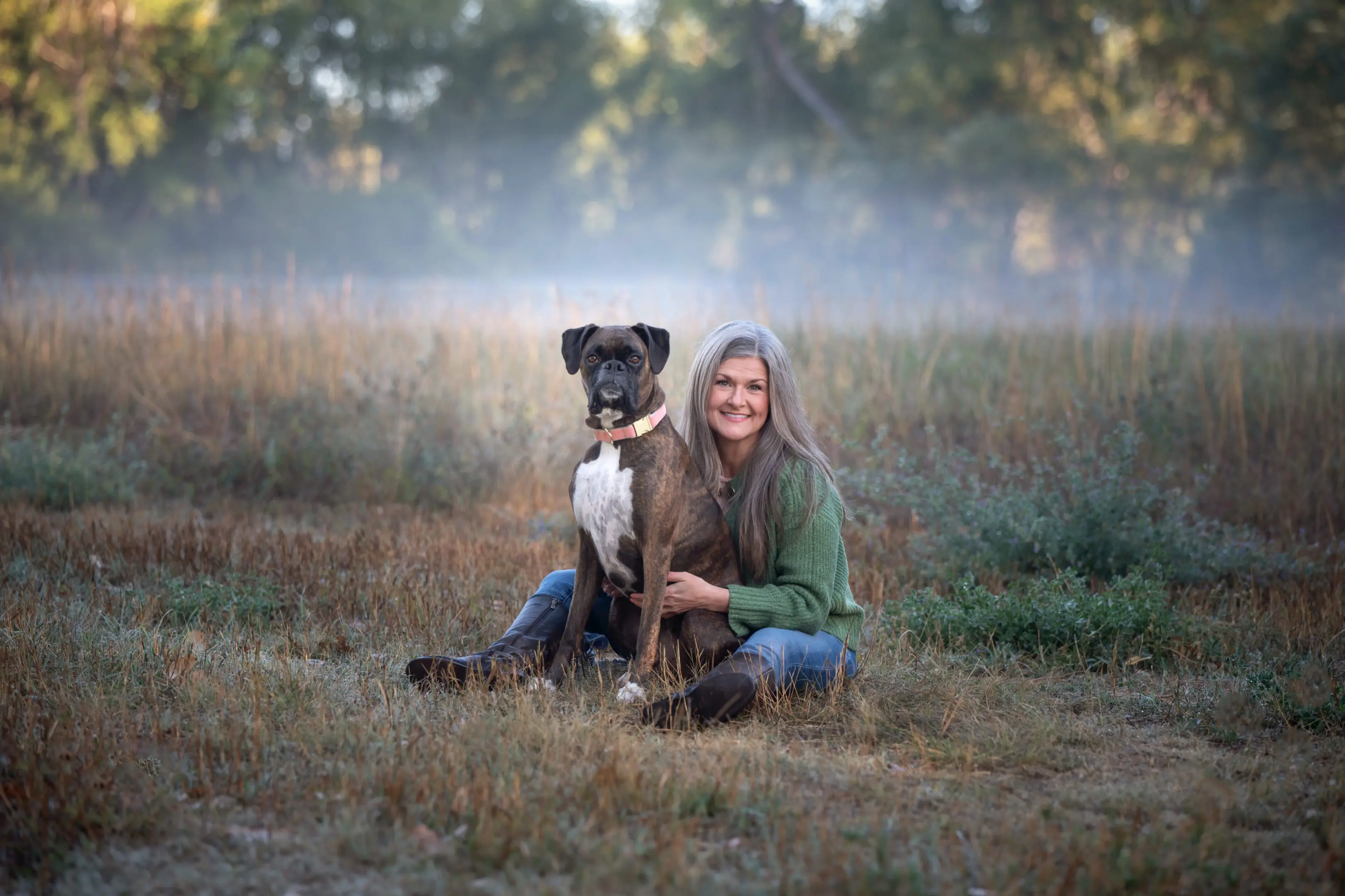 A woman sitting on grass with a large dog in a foggy field.