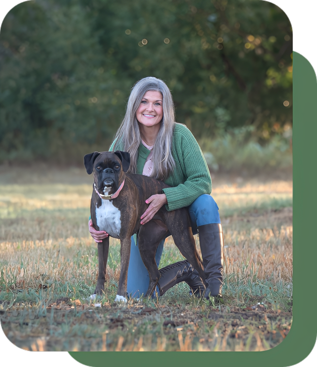 Smiling woman in green sweater with her black and white dog outdoors.