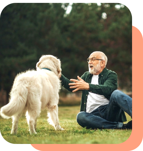 An elderly man joyfully playing with a white dog outdoors.