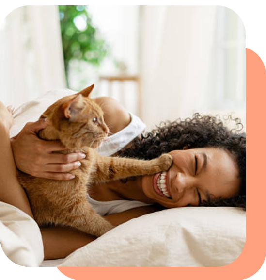 Woman joyfully cuddling her orange cat on a bed.