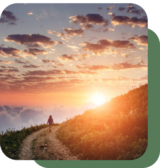 A person walking on a hill path during a vibrant sunset.