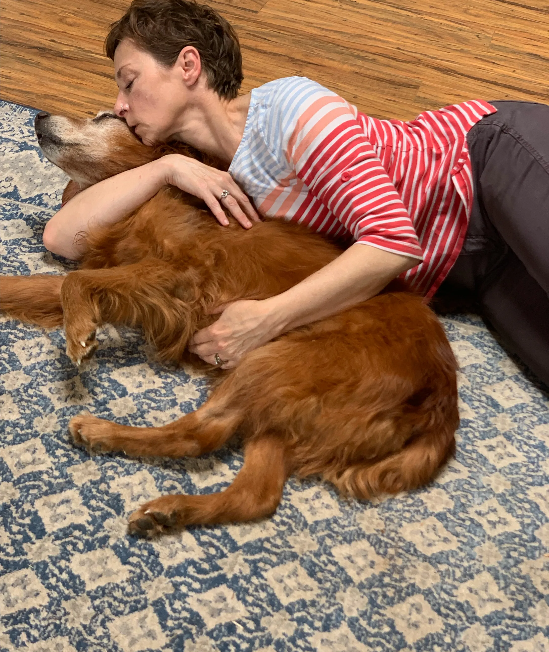 Woman lying on a rug cuddling a large dog.