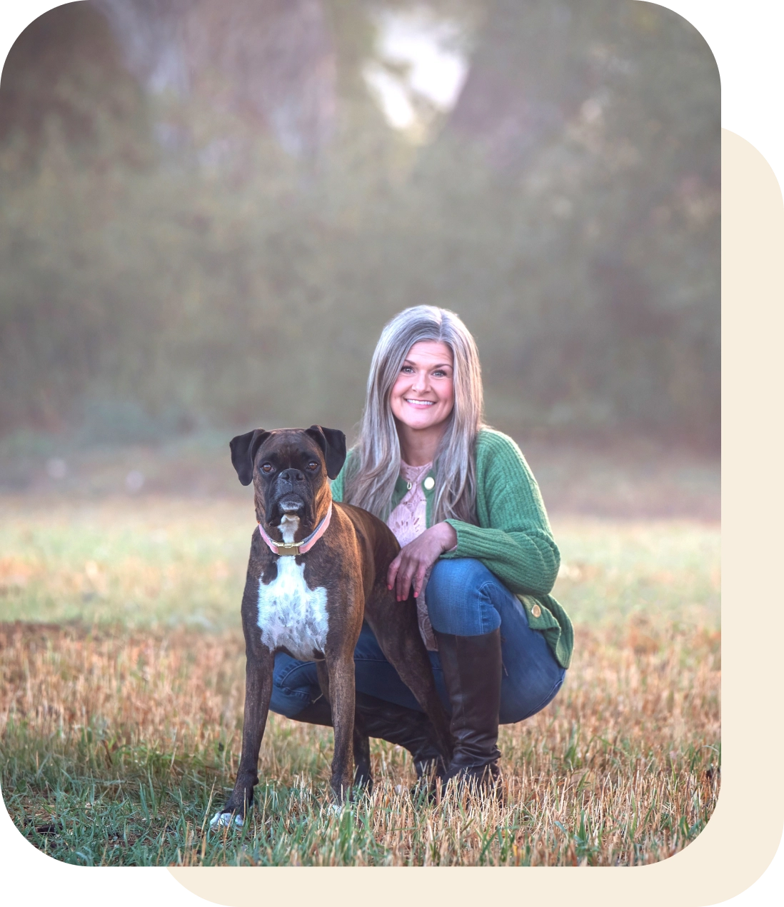 A woman kneeling beside a large dog in a grassy field during sunset.